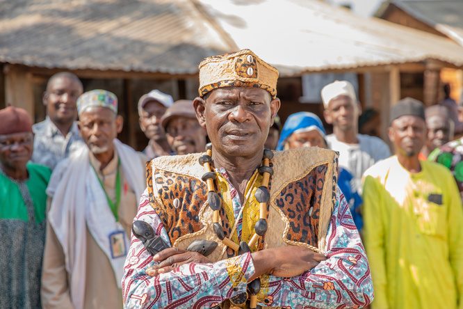 A man in colourful robes with his arms crossed stands in front of a group of people