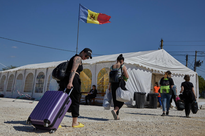 People carrying bags and pulling suitcases walk towards a large tent with a Moldovan flag flying above it
