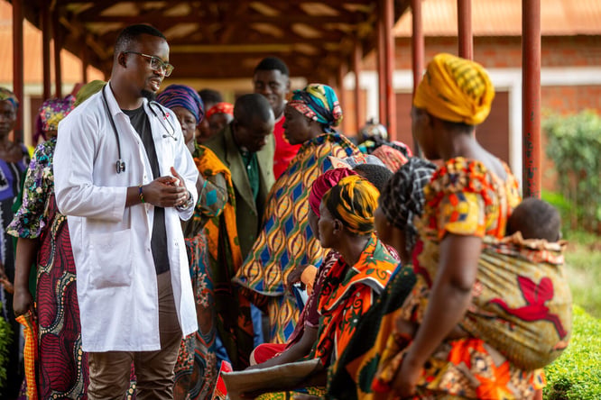 A clinician in a lab coat meets with a group of people outside.