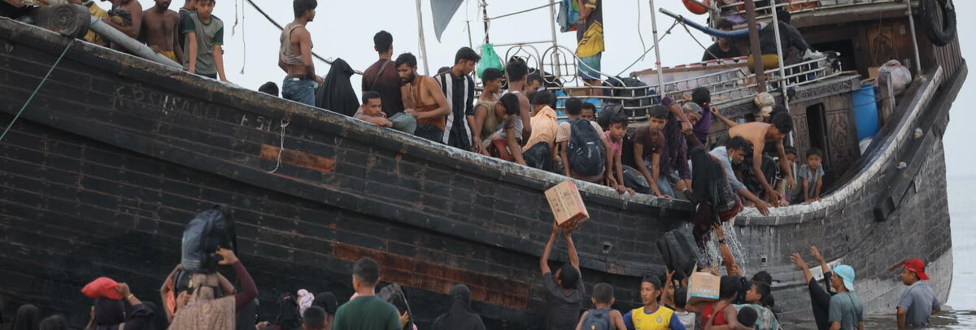 Rohingya refugees disembark from a crowded boat into shallow water