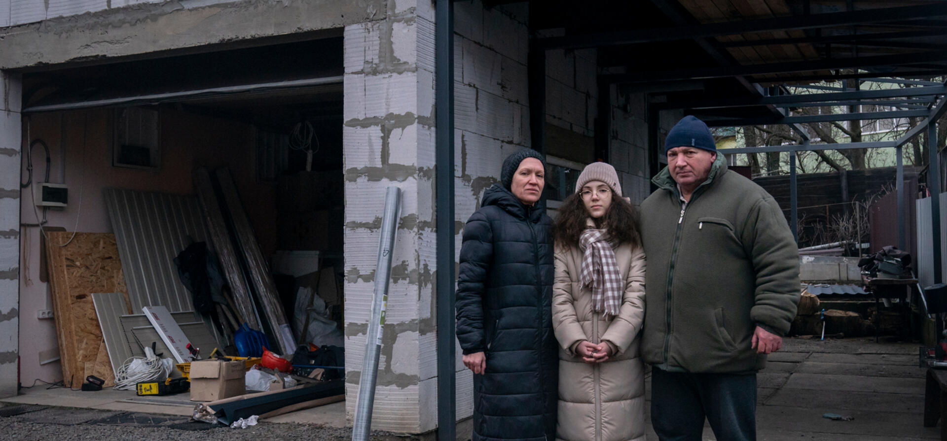 A couple and their daughter stand in the yard of their recently repaired home