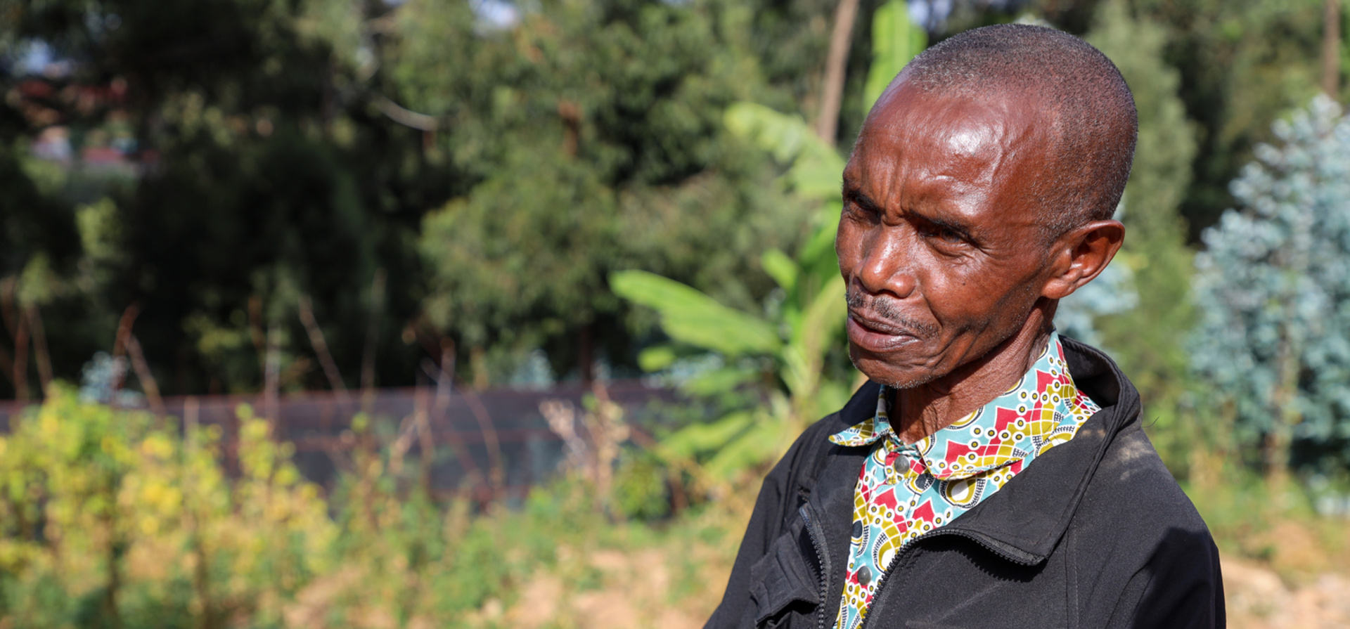 A man stands in front of a nursery of tree seedlings in a refugee camp.