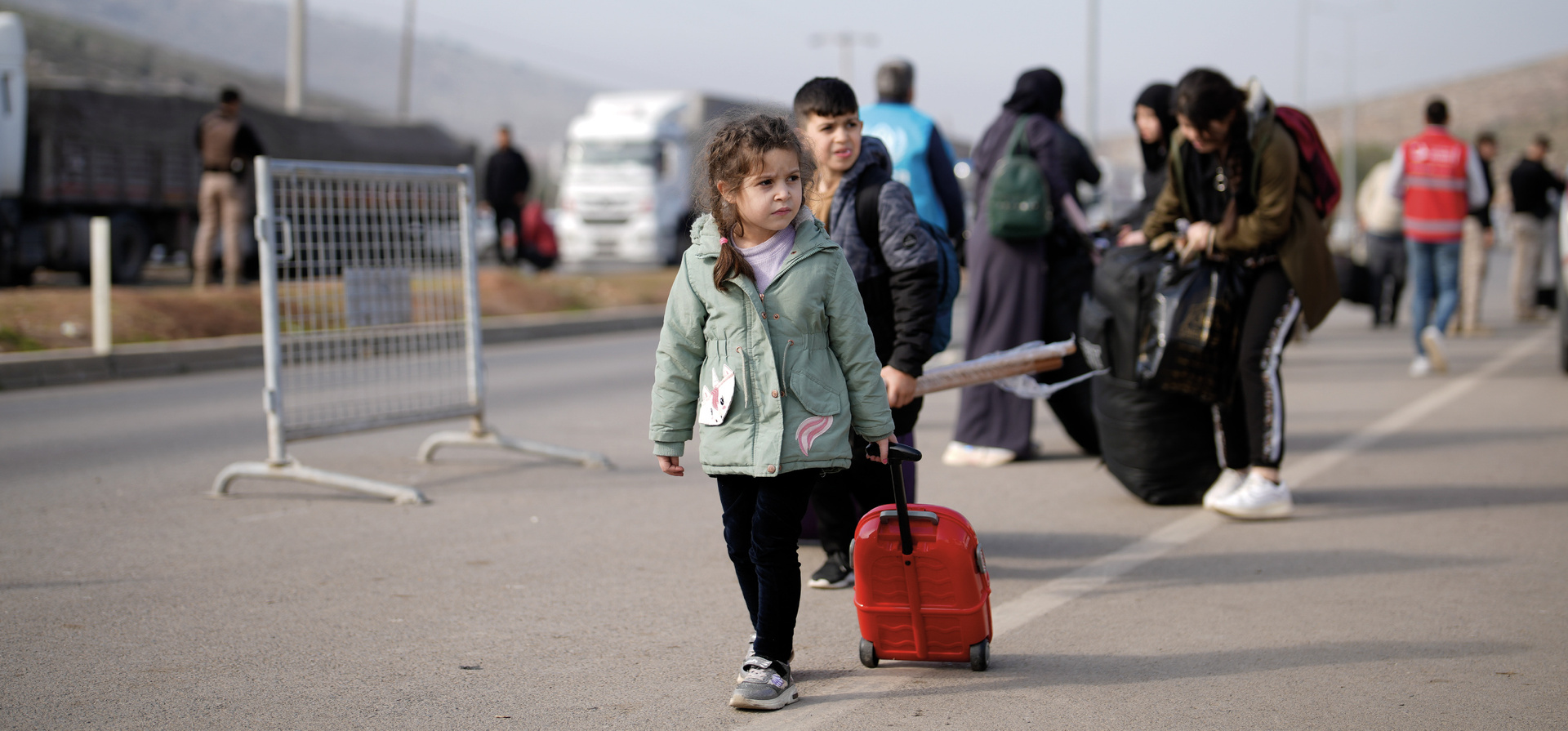 A young child walks on asphalt pulling a small suitcase.
