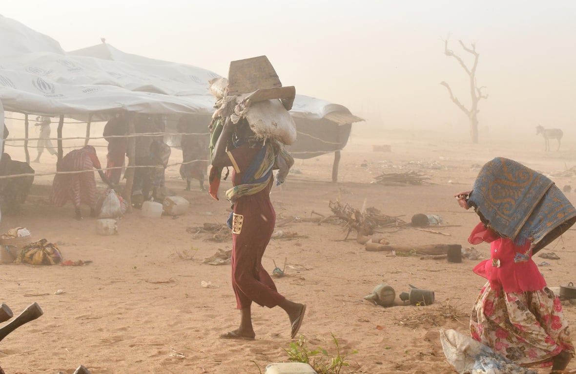 A woman and a child carry their belongings as they seek shelter during a sandstorm.