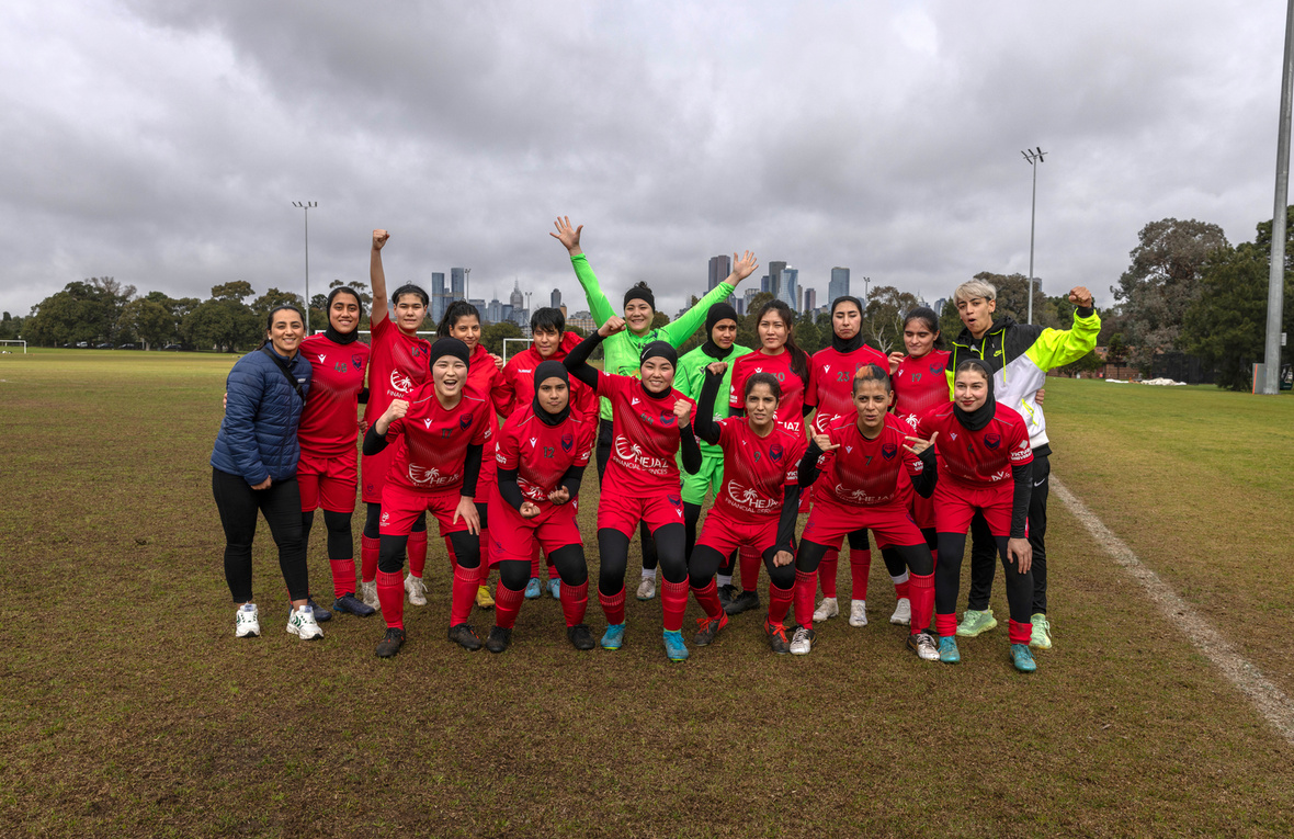 A women's football team gathers for a group portrait on a football field.