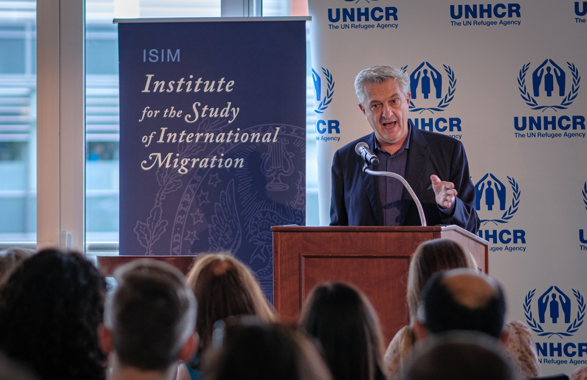 Filippo Grandi speaks from a podium in front of a UNHCR banner and next to a banner which says 'Institute for the Study of International Migration'
