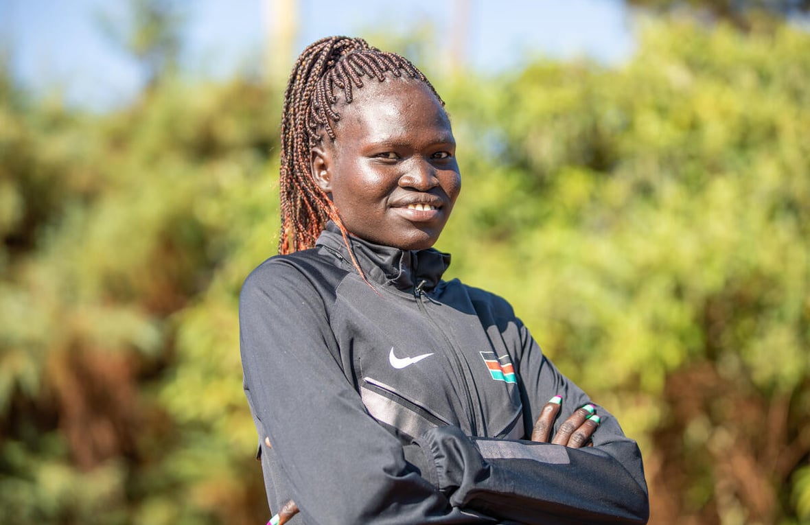 A young African woman wearing a tracksuit poses for a portrait in front of trees.