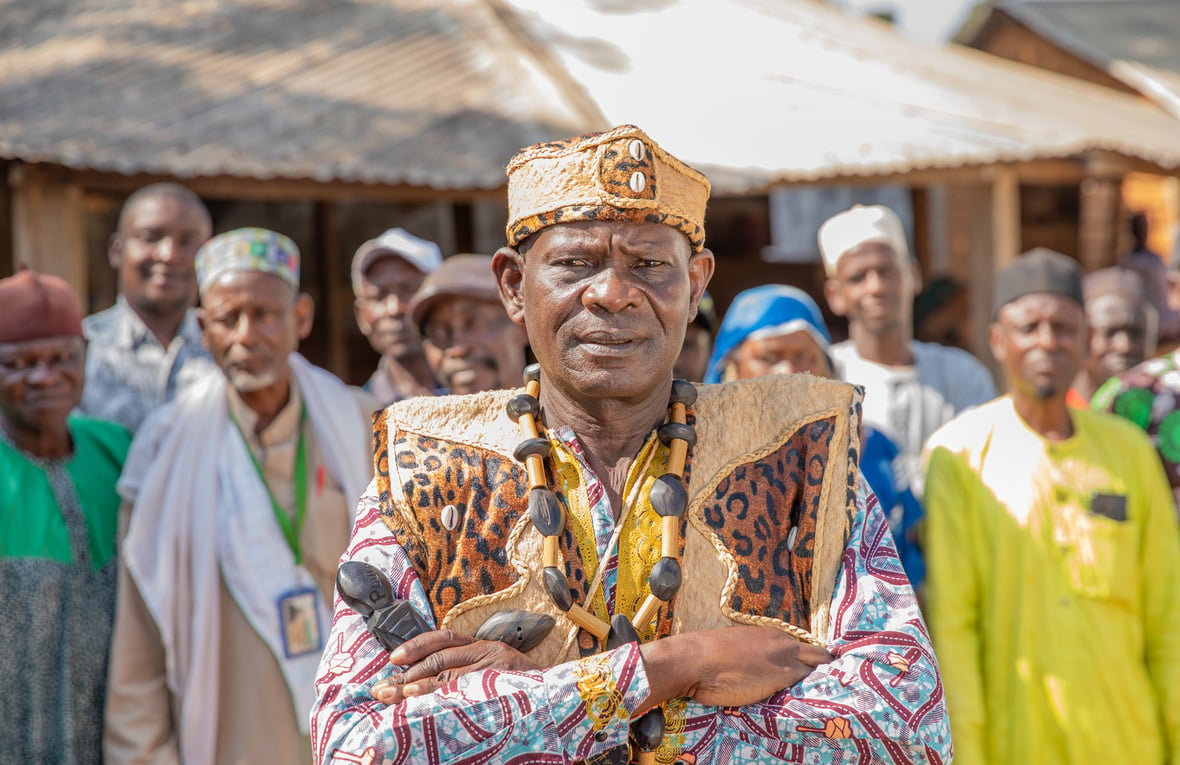A man in colourful robes with his arms crossed stands in front of a group of people