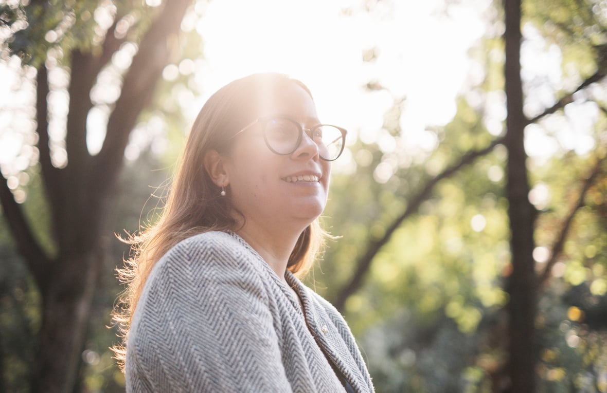 Sunlight shines through trees onto a woman wearing glasses and a business jacket 