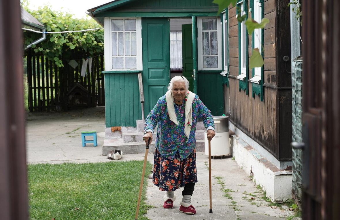 Une femme âgée dans la cour de sa maison, s'aidant de deux cannes