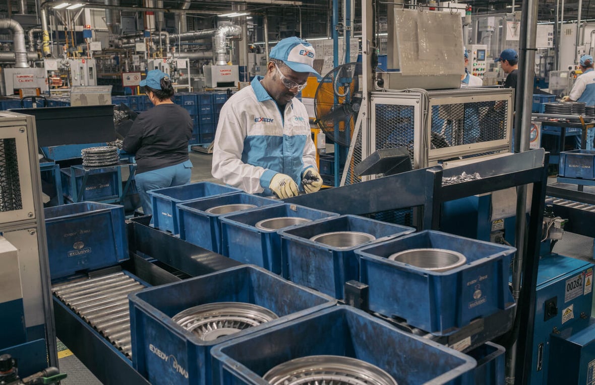 A man wearing overalls, protective eyeglasses and a cap works in an auto parts factory