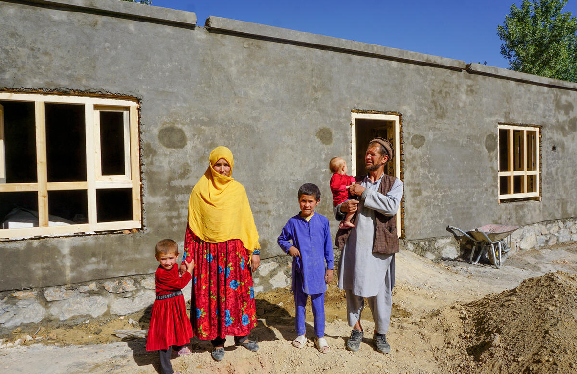 A man holding his child stands with his wife and two children in front of a newly built apartment.