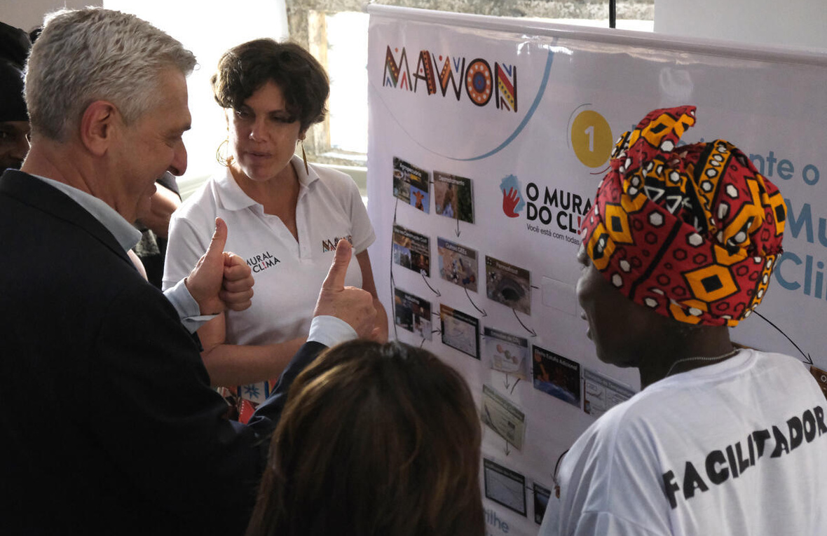 Two women and a man talk in front of an exhibition panel.