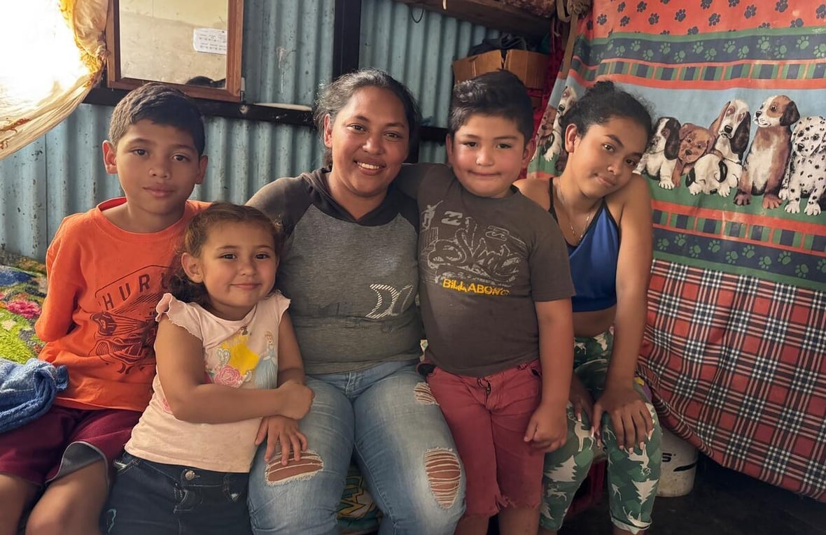 A mother sits on a bed in a shack with her four children.