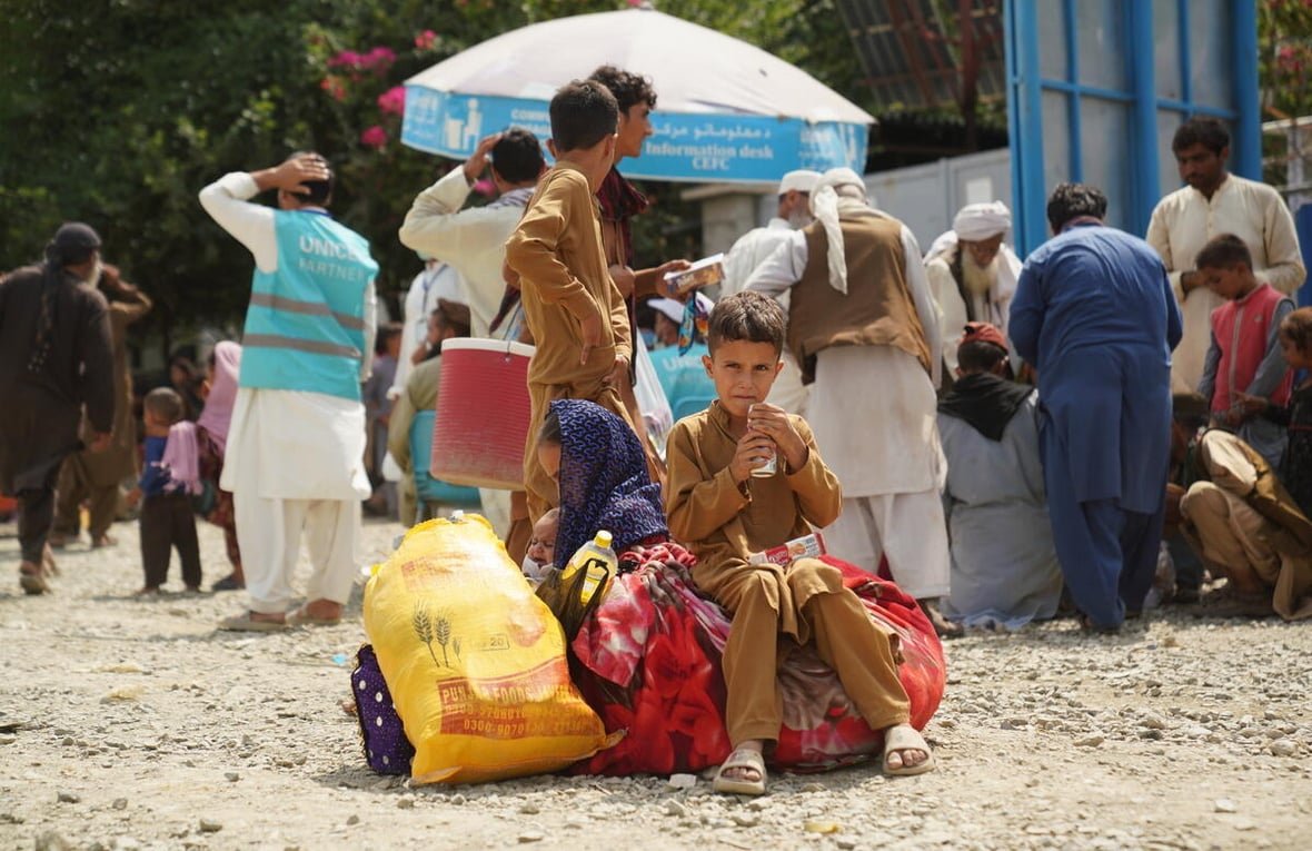 A young Afghan boy sits on piles of luggage, while others stand behind.