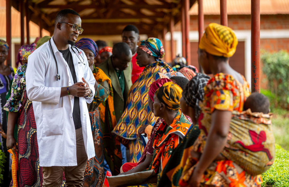 A clinician in a lab coat meets with a group of people outside.