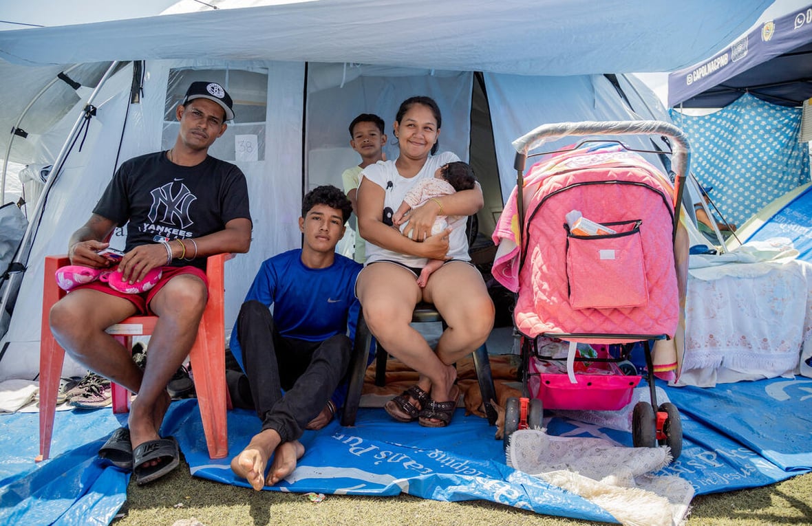 A family sits outside the entrance to a tent