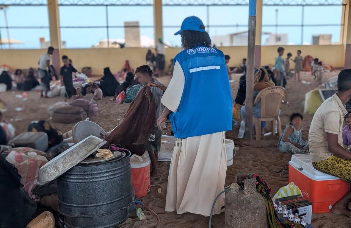 UNHCR staff support displaced families gathered in a large shelter with a sand floor