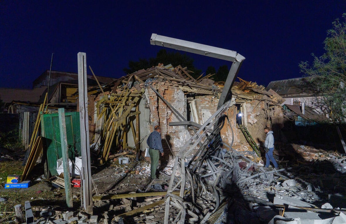 Two people assess damaged and collapsed buildings.
