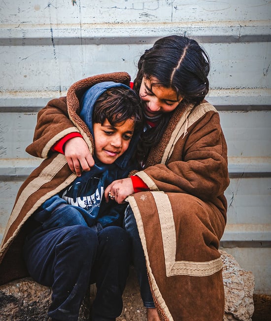 طفلة سورية لاجئة شابة تتلحف بطانيةً مع شقيقها الأصغر وهما يجلسان في البرد القارس في مخيم الزعتري للاجئين.