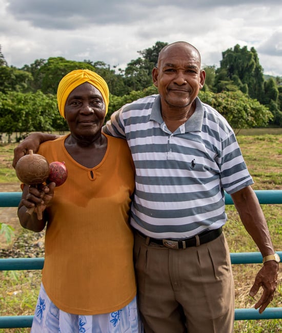 Elderly refugee couple stands in front of a field.