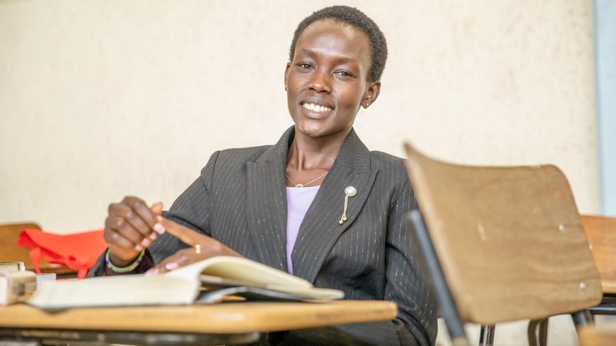 A young woman smiling and sitting at her desk in a classroom
