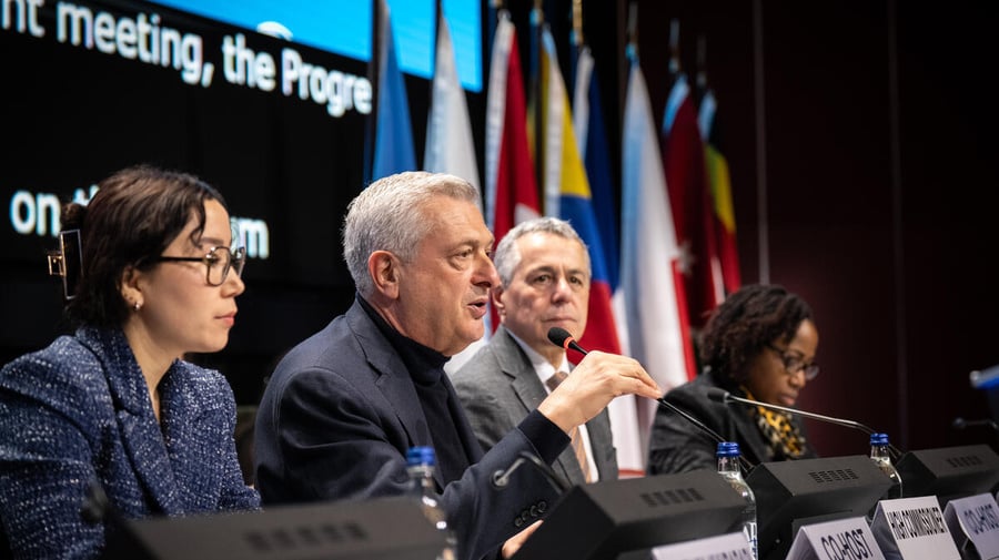 Four persons sitting on stage, one of them speaking into a microphone