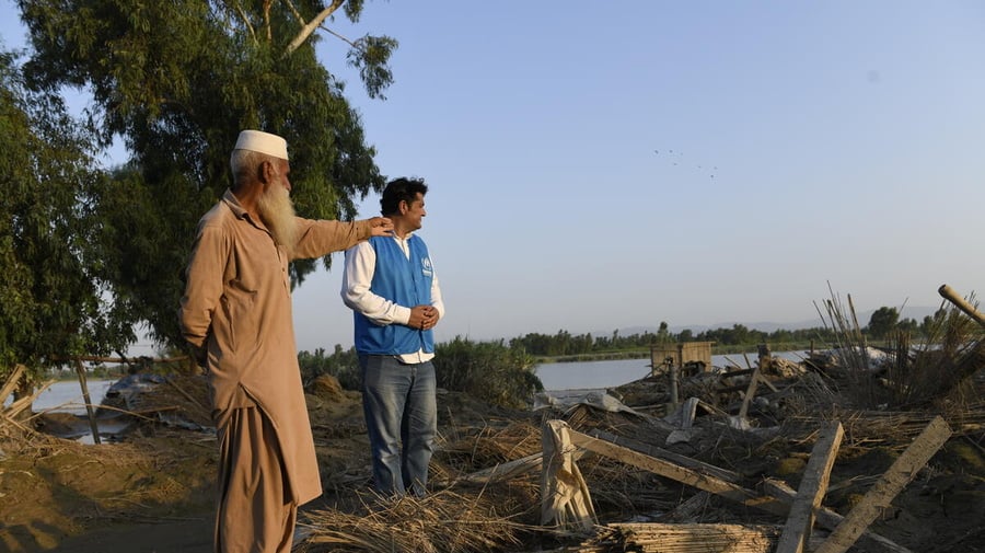An Afghan man gestures to a UNHCR worker, showing devastation caused by a monsoon.