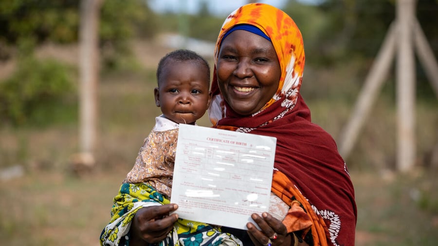 A woman holds her baby and proudly displays a birth certificate.