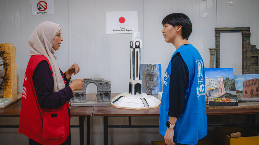 A Syrian refugee volunteer and a UNHCR Associate Programme Officer stand together talking in a community centre.