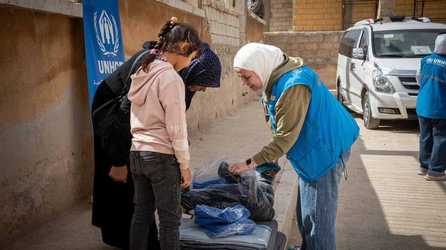 A child, an adult and a UNHCR staff member look through a UNHCR winter kit
