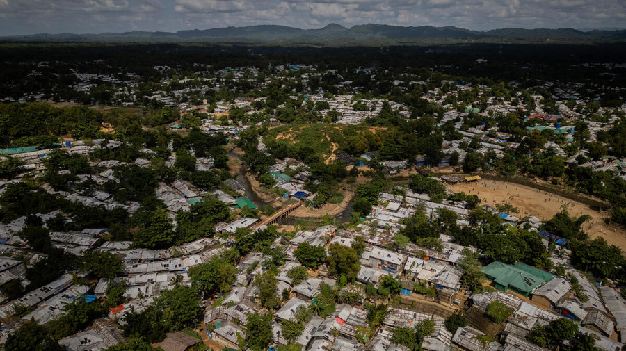 An aerial view of a huge refugee camp, trees throughout, with mountains in the background