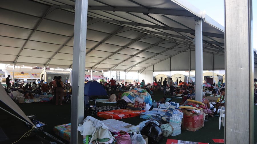 A temporary shelter filled with supplies and people in the background