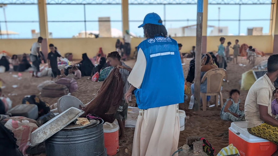 UNHCR staff support displaced families gathered in a large shelter with a sand floor