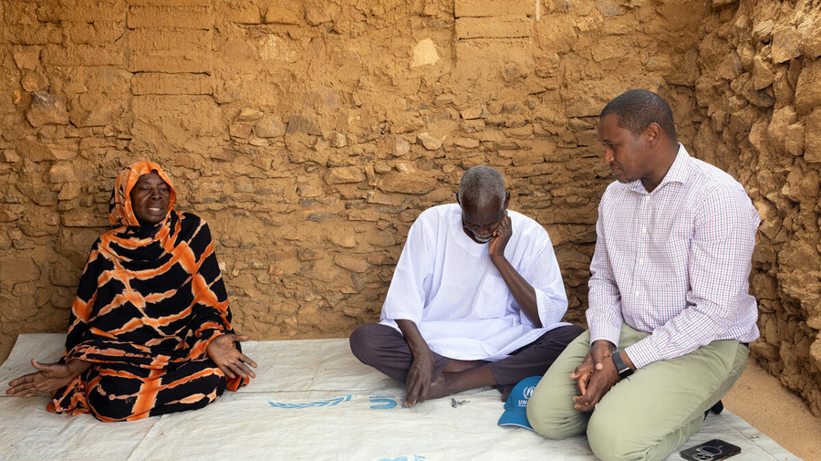 Mamadou Dian Balde sits on the floor, speaking with two Sudanese refugees.