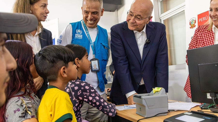 Barham Salih and UNHCR colleagues speak with a family sitting behind a desk with a computer. Everyone is smiling.