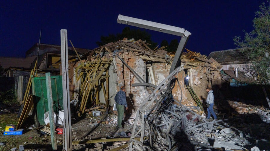 Two people assess damaged and collapsed buildings.
