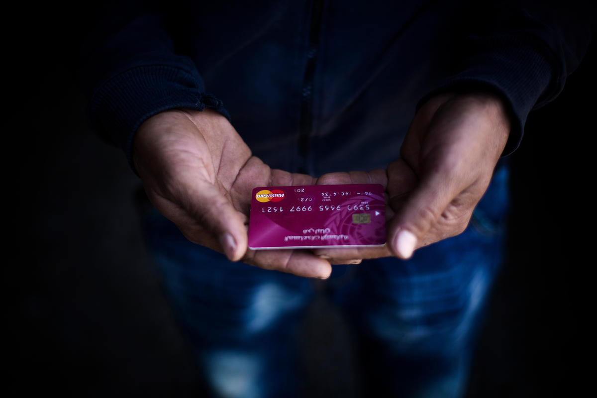 A young Syrian refugee holds an ATM card provided by UNHCR inside a distribution point in Tripoli, Lebanon, April 2018. She will use the cash to provide for her daughters, aged four and six.