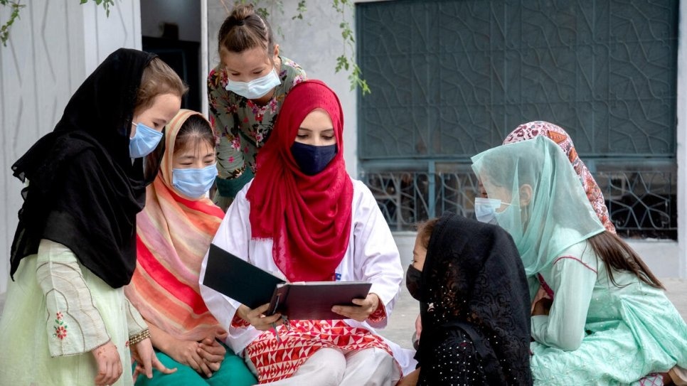 Saleema翻開相簿觀看舊照，向一些難民女孩講述她成為醫生的旅程。 © UNHCR/Amsal Naeem