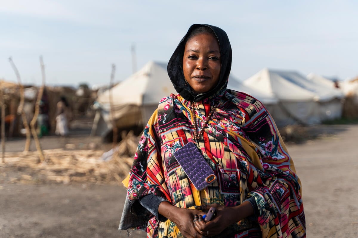 A woman in a colourful dress stands in front of rows of white tents in an IDP camp.