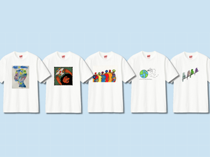 Five white t-shirts with unique artistic designs: one featuring a person painted with watercolors, another depicting a person with a dove, a third displaying a group of people, a fourth showcasing the Earth with a paper airplane, and the fifth has a design of four birds in a line.