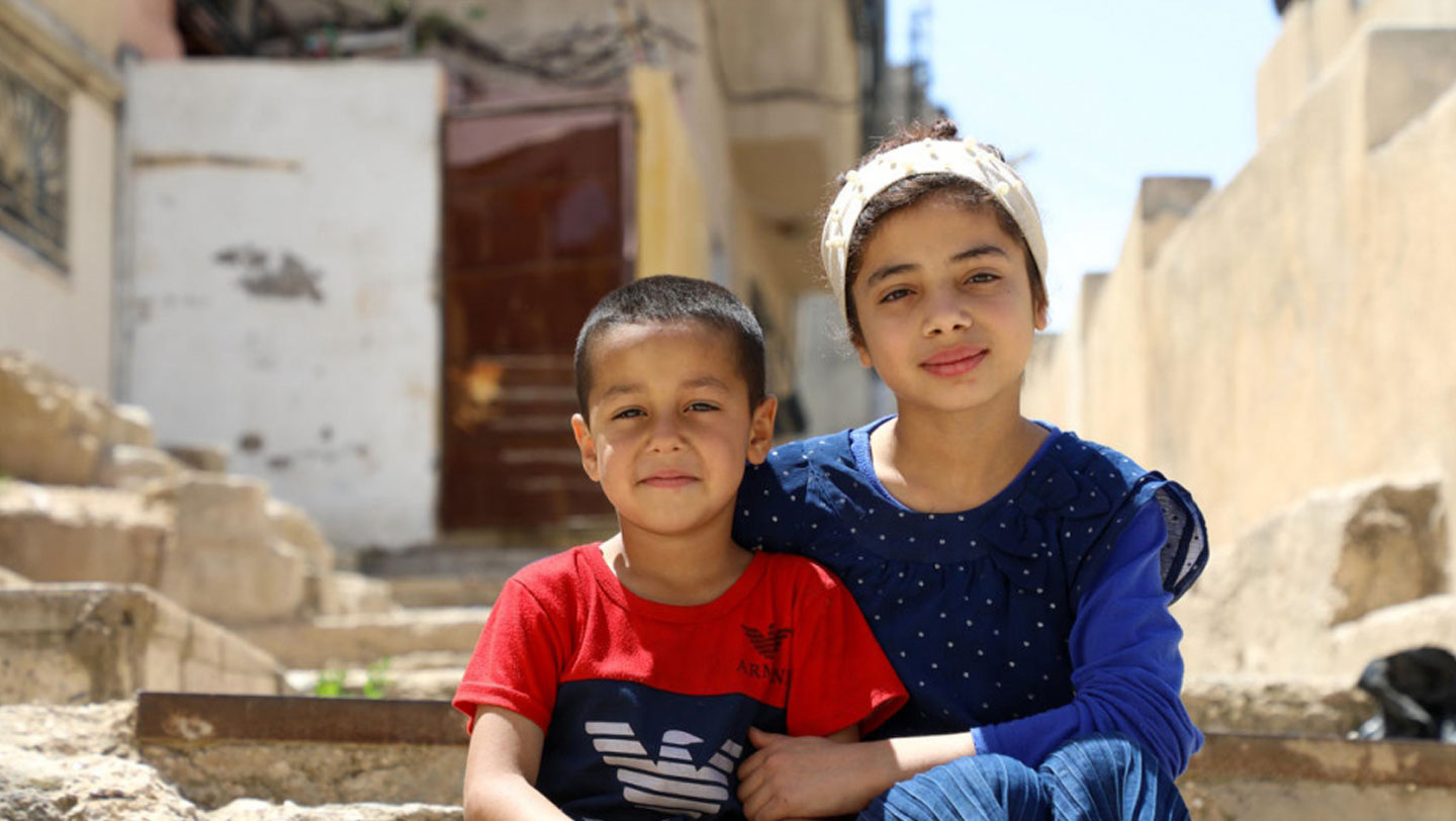 Nadia, 12, and her youngest brother Abed, 5, sit in the alleyway outside their home in East Amman. They and their three other siblings have been taking turns using the family’s one TV and mobile phone. © UNHCR/Lilly Carlisle