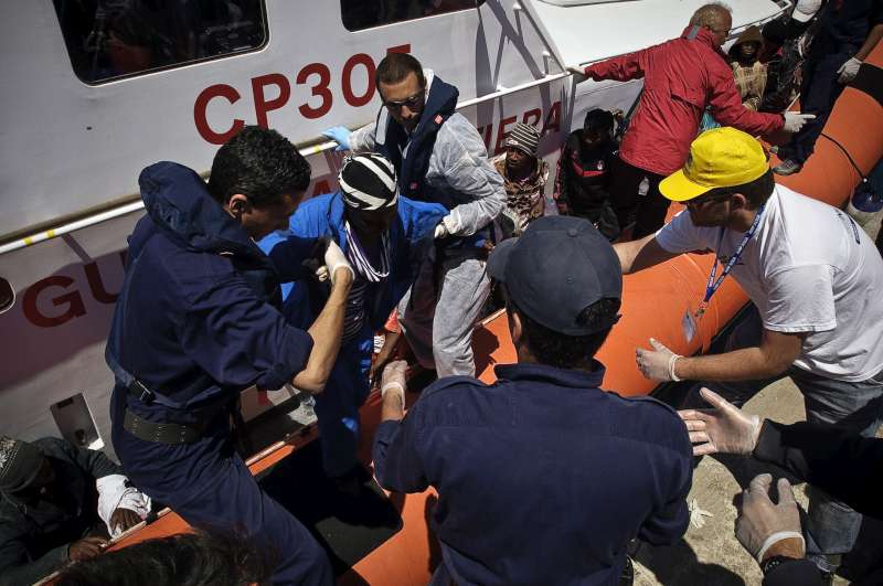 An injured man from sub-Saharan Africa is helped off an Italian coastguard vessel after being picked up at sea. He had fled from Tripoli with others. 