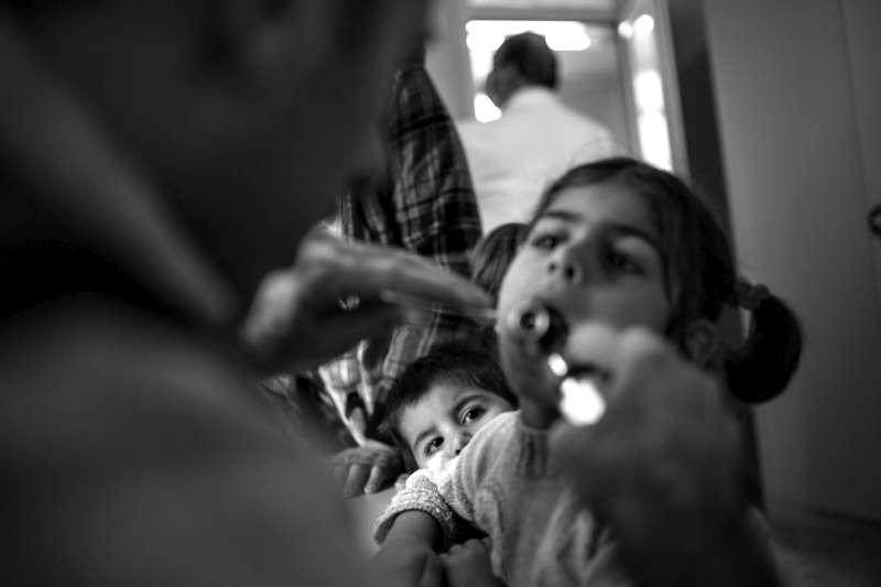 A doctor examines a sick Syrian refugee girl while her younger brother looks on at a health clinic in Domiz Refugee Camp.