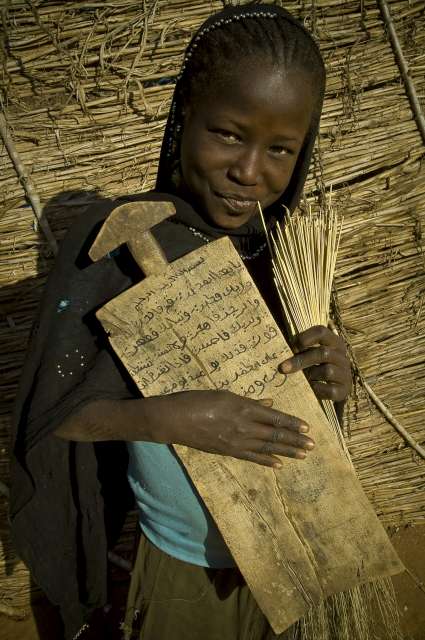 A young Sudanese refugee student on her way back to her family's simple shelter after attending classes at a madrassa (Islamic school) in Djabal camp, eastern Chad. She carries an alluha, a small wooden board on which she writes her lessons. 