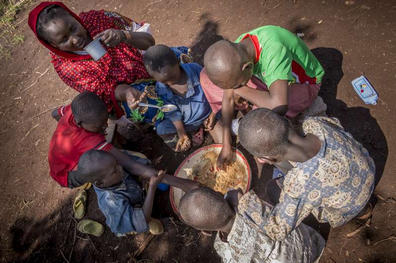 Six hungry boys tuck into a bowl of food as Ramatou sips water from a cup in Mbile Refugee Camp.