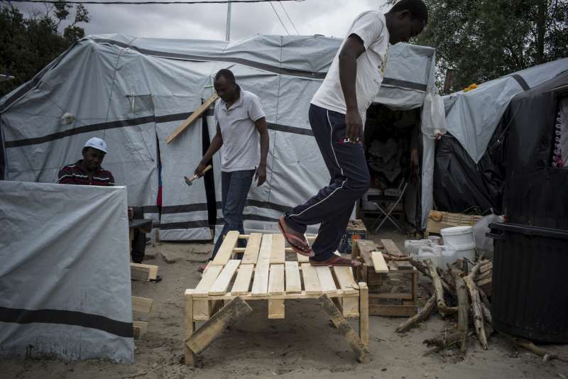 Sudanese refugees and migrants build a bed in front of their shelter.