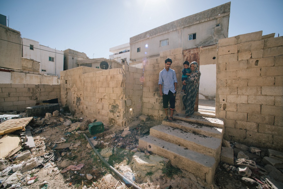 Syrian refugee Aisha holds her son Hamzah, 2, while standing next to her brother, Mohammad, 16, outside of their house in Karak, Jordan.