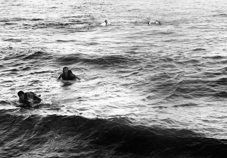 Survivors struggle ashore after their boat had capsized. In the background a Spanish lifeguard swims out to help other survivors.
