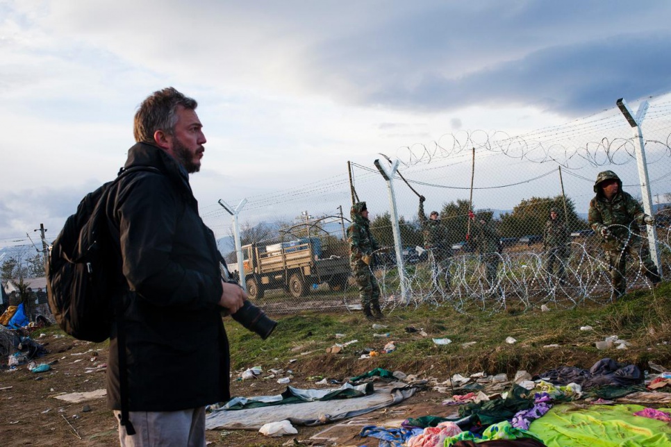 Giles Duley stands on the no-mans land near the Greece-FYROM border while soldiers erect a metal fence.